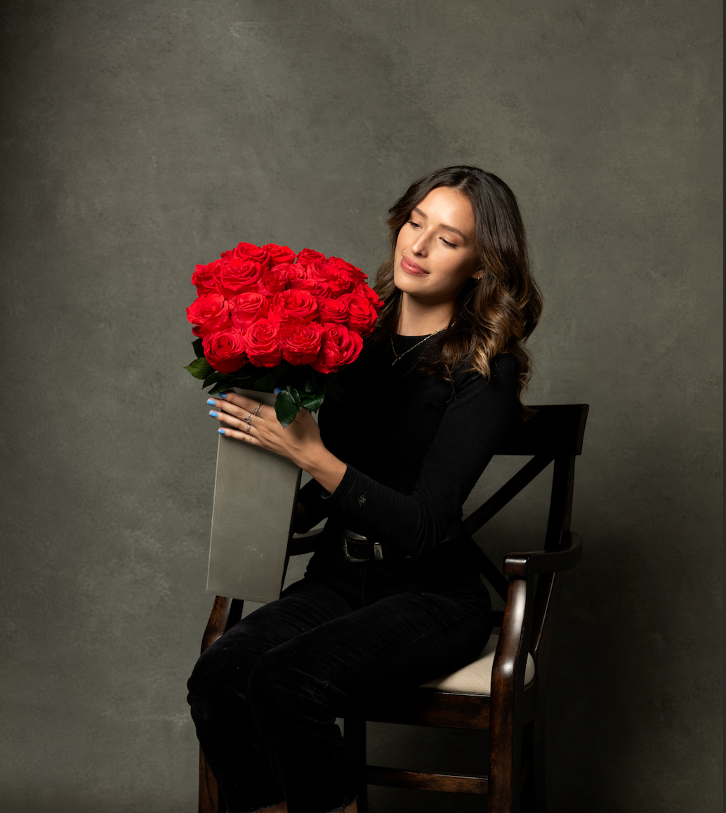 A woman in black seated in a studio, holding a large bunch of red preserved roses.